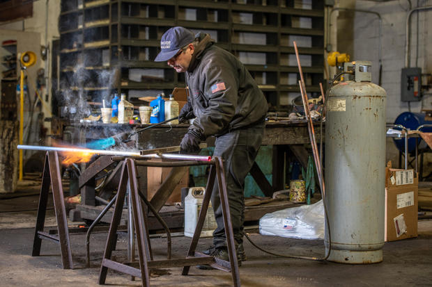 Man holds light blowtorch to heat up copper tube to anneal it at metal bending shop, Dundalk, MD